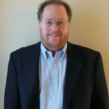 Man in suit jacket and glasses smiling at camera.