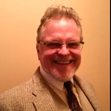Smiling man in glasses and a suit jacket.