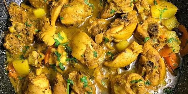 A pot of curried chicken with carrots and potatoes garnished with herbs.