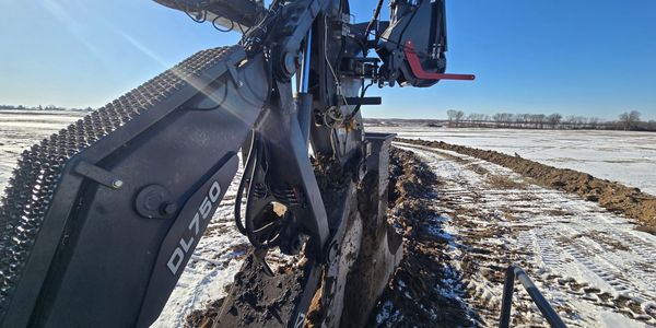 Excavator digging in a snowy field under a clear blue sky.