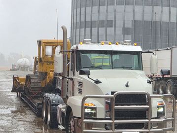 White semi truck carrying yellow heavy machinery.