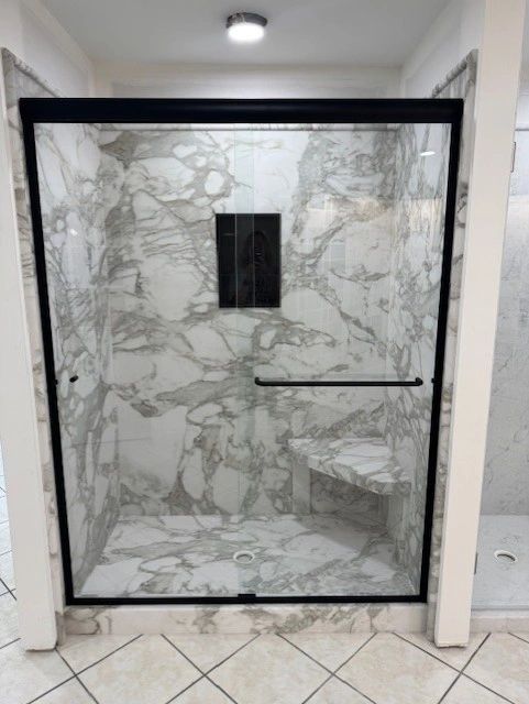 Modern marble shower with glass door and bench.