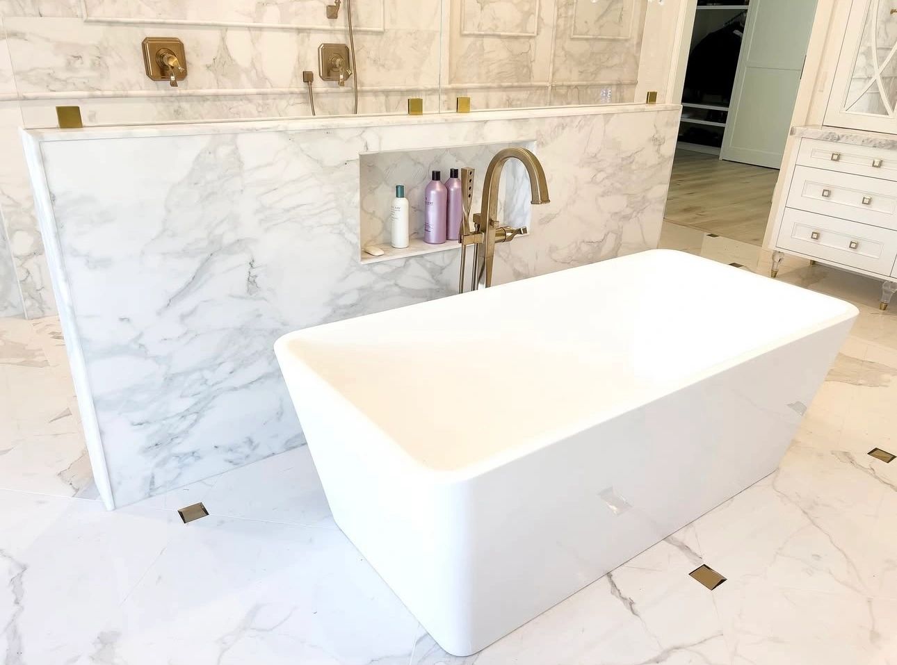 Modern white bathroom with marble tiles and a freestanding bathtub.