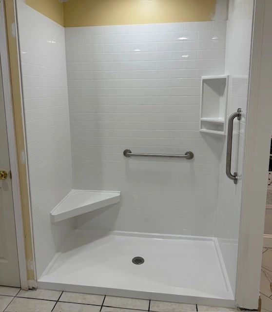 Newly renovated white tiled walk-in shower with safety bars and a seat.