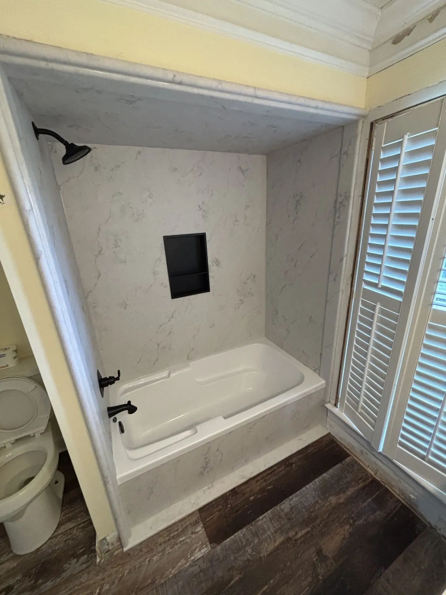 White bathtub with marble walls and wooden floor.
