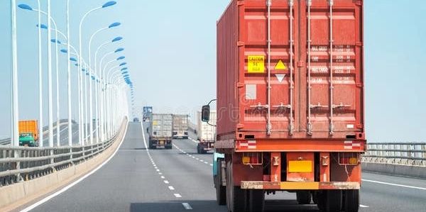 Red cargo truck driving on an empty highway under clear sky.