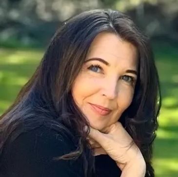 Woman with long dark hair posing outdoors with a gentle smile.