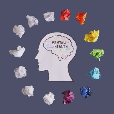 Paper head with words on mental health surrounded by colorful crumpled papers.