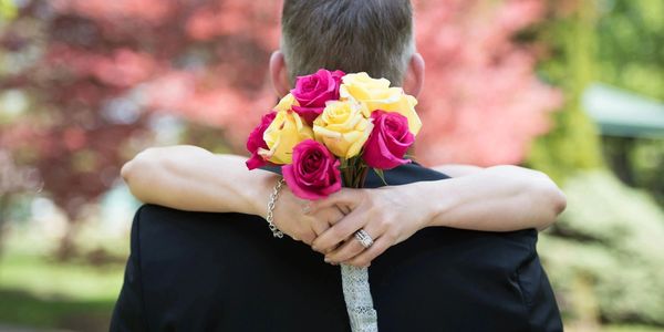 Bride embraces groom holding a bouquet of roses.