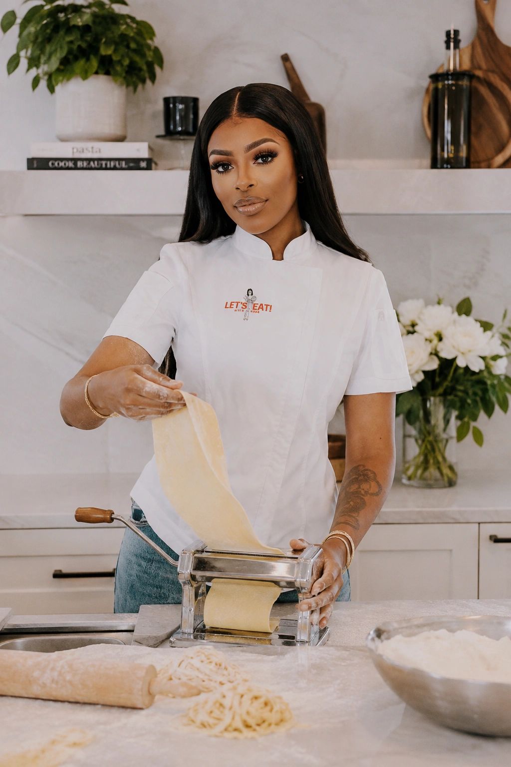 Woman making pasta using a rolling machine in a kitchen.