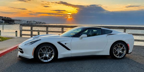White sports car parked near a waterfront at sunset.