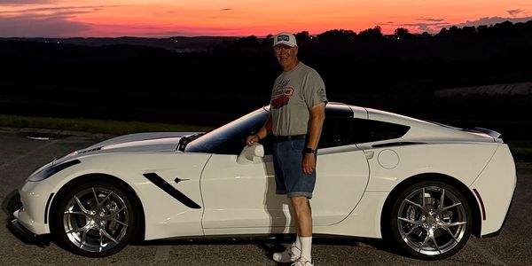 Man posing with a white sports car at sunset.