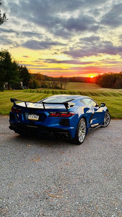 Blue sports car parked at sunset in a scenic field.