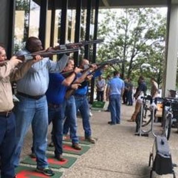 People aiming rifles at an outdoor shooting range under a covered area.