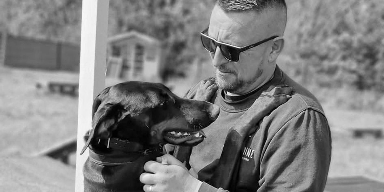 Trainer interacting affectionately with a Doberman during a training session outdoors, highlighting trust and bonding in a structured canine training environment.