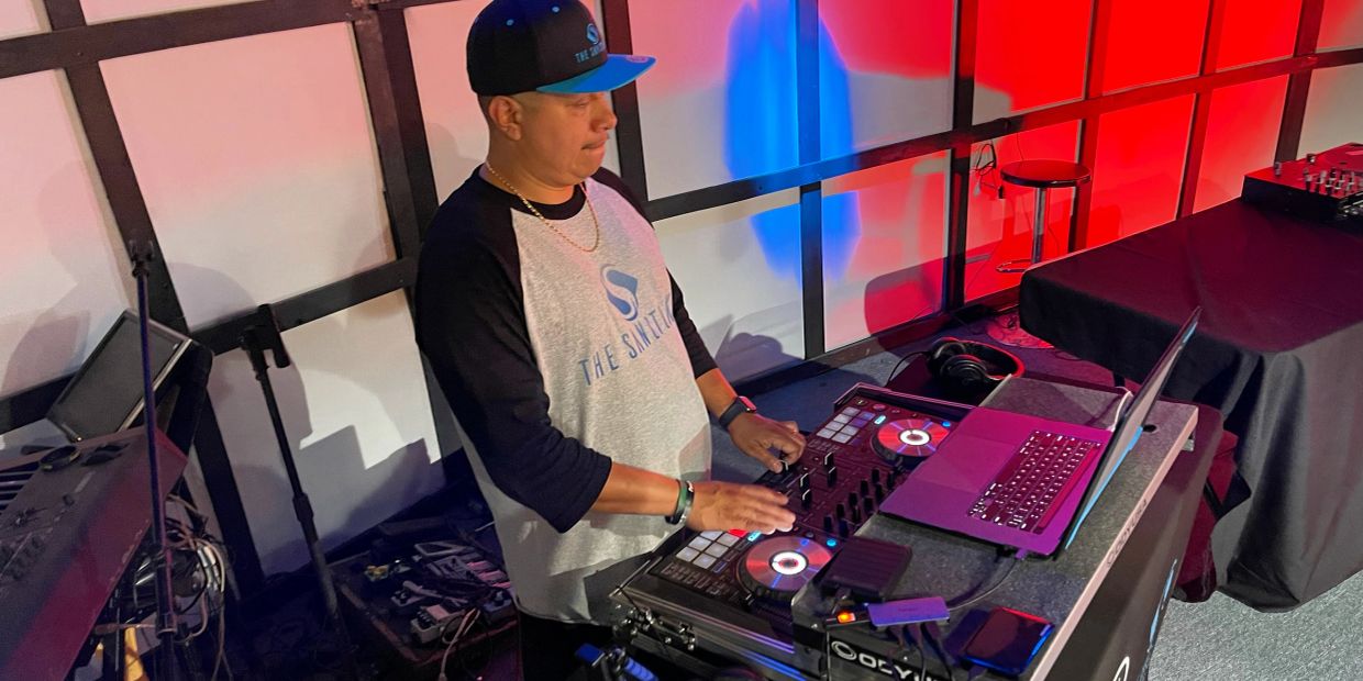 A DJ mixing music on a controller with a laptop in a colorful room.