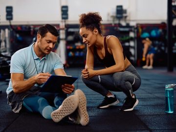 A fitness coach discusses a workout plan with a female athlete in a gym.