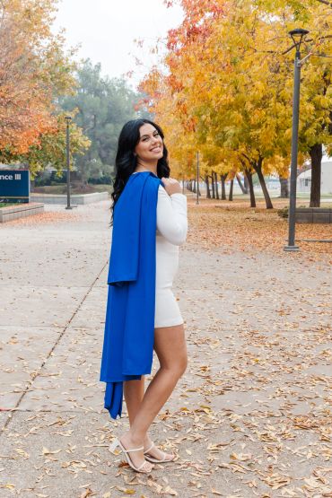 Woman in white dress with blue graduation stole outdoors in fall.