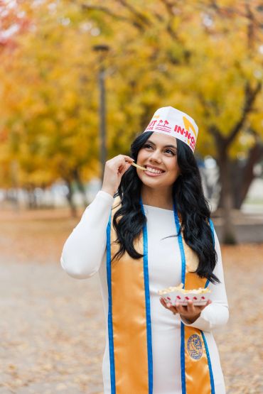 Graduate happily eating fries outdoors in autumn.