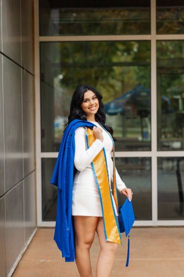 Young woman in white dress holding a blue graduation gown and cap.