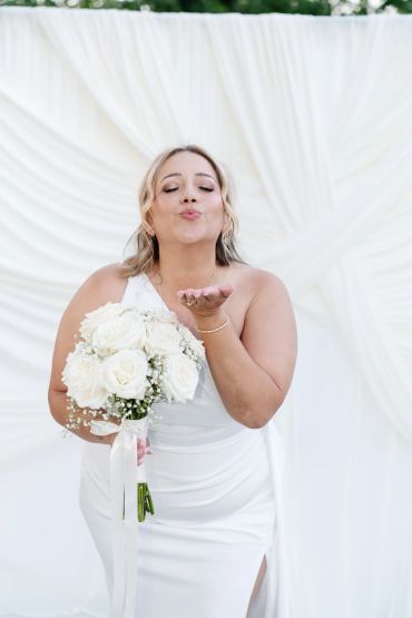 Bride blowing a kiss holding white rose bouquet.