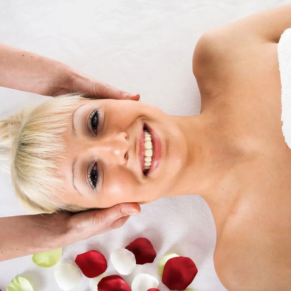 Woman enjoying a relaxing facial massage with rose petals nearby.