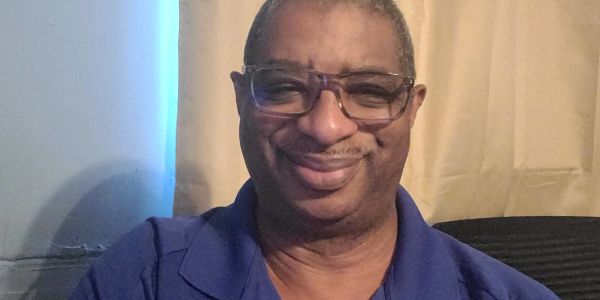 Man smiling indoors, wearing glasses and a blue shirt.