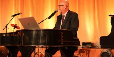 Man in suit playing piano and singing into microphone on stage.