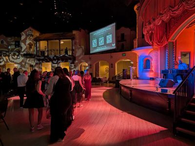 People waiting in line inside a dimly lit, colorful theater with QR codes on a screen.