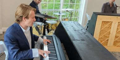 A man in a suit plays piano with two other musicians nearby.