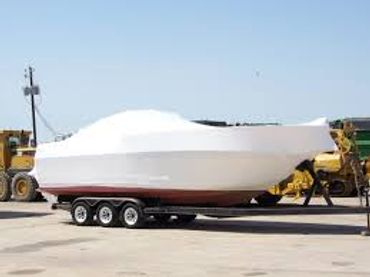 A large boat covered in white protective wrap on a trailer.
