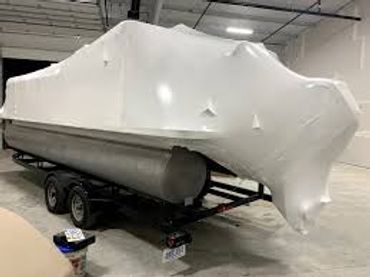 Boat wrapped in white shrink wrap on a trailer indoors.