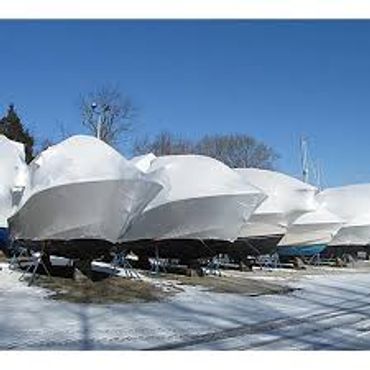 Boats covered in protective white tarps during winter under a clear blue sky.