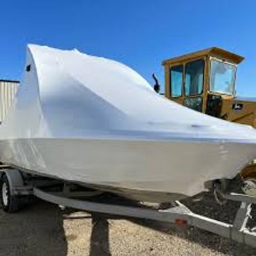 Boat covered with a white protective tarp on a trailer.