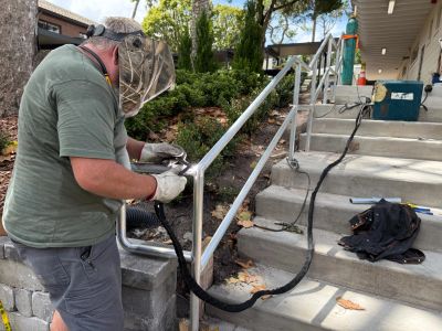 Man welding metal railing on outdoor stairs.