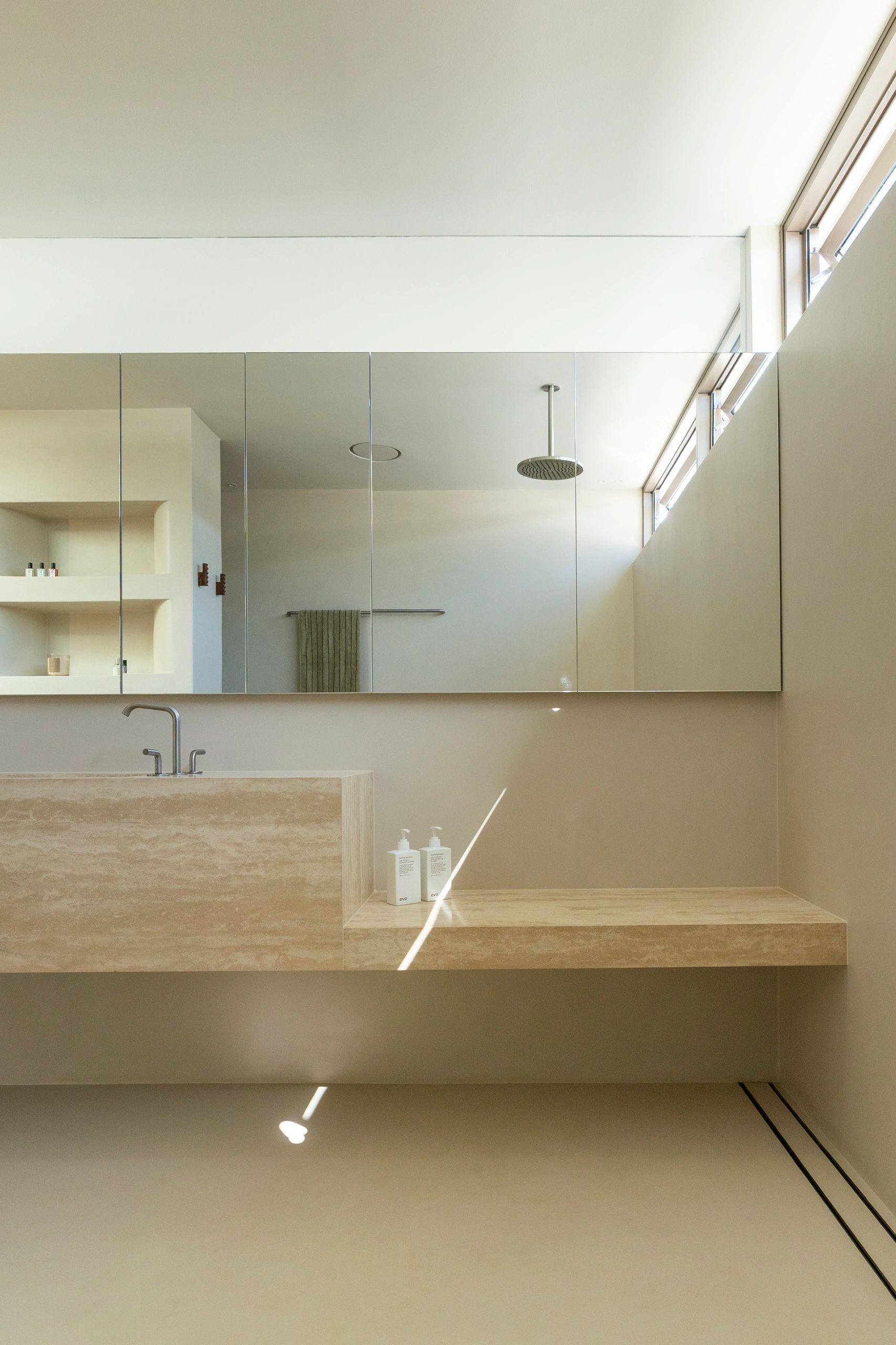 Minimalist beige bathroom with large mirror and natural light.