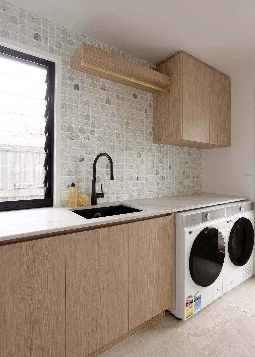 Modern laundry room with wooden cabinets and tiled backsplash.