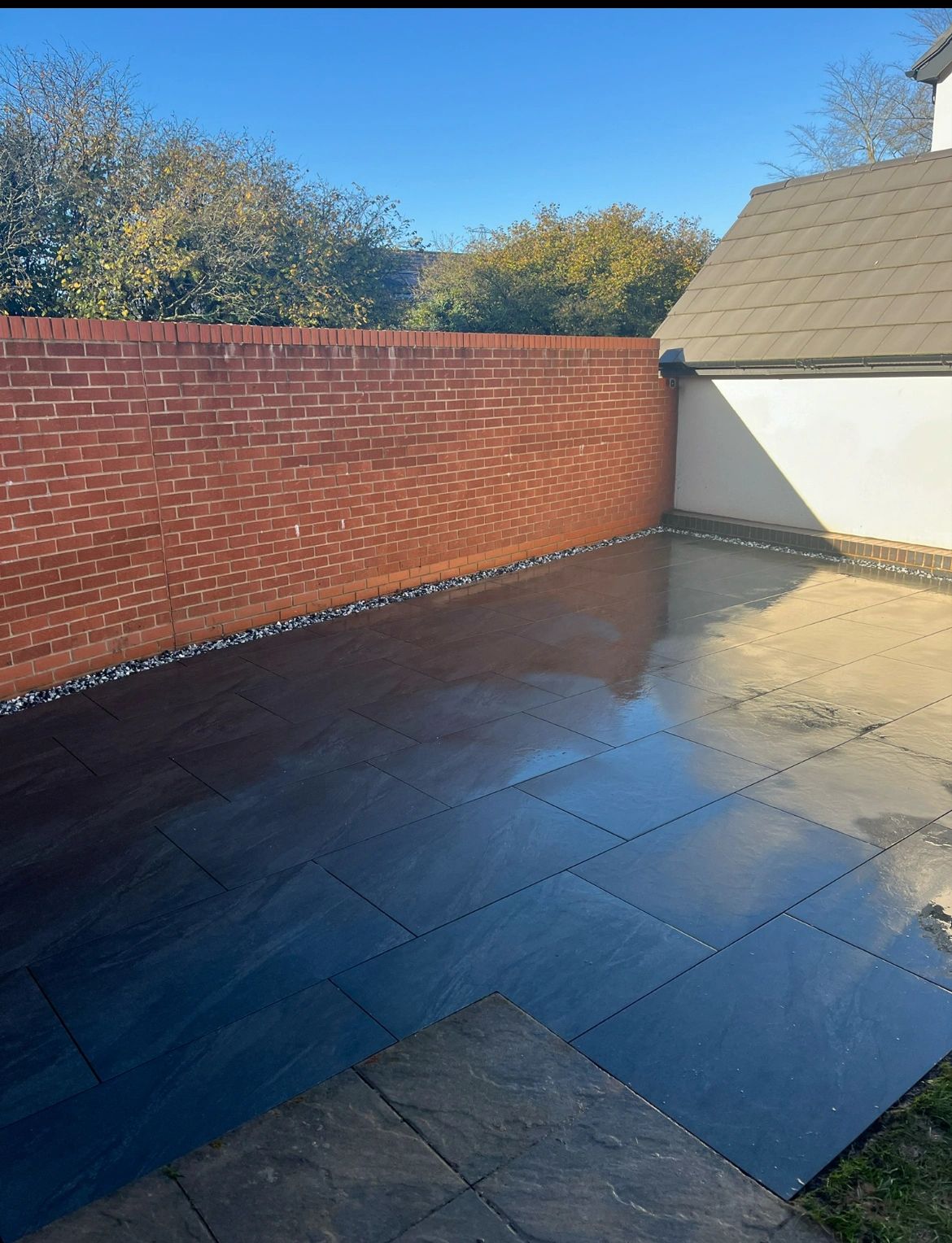 A clean, newly tiled patio with a brick wall and clear blue sky.