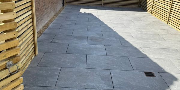 A clean backyard patio with stone tiles and wooden fencing.