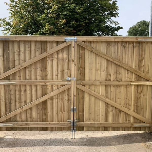 A wooden double gate with metal hinges and braces in a fenced area.