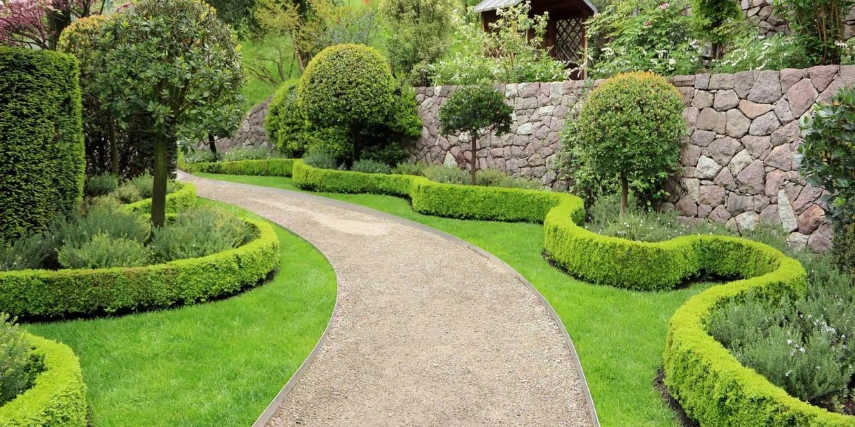 Curved garden path lined with neatly trimmed hedges and topiary trees.