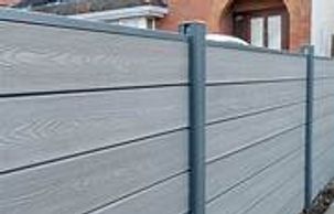 Modern gray composite fence panels with metal posts outside a brick house.