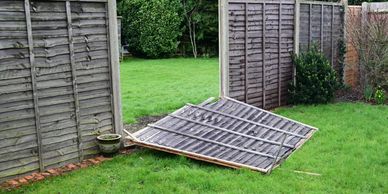 A broken wooden fence panel lies on green grass in a garden.