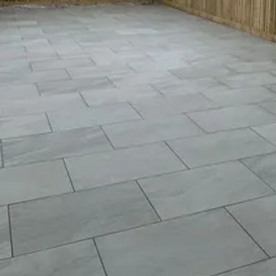 Newly paved patio with light gray tiles and wooden fencing.