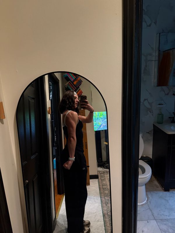Person flexing arm muscles in front of a mirror in a hallway.