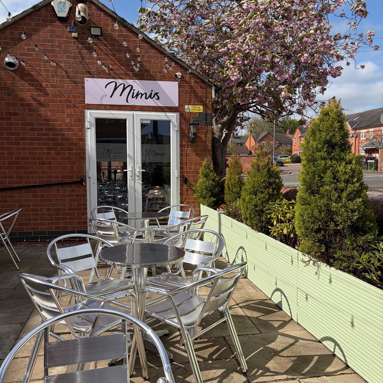 Outdoor seating area at Mimi's café with metal chairs and tables under a blossoming tree.