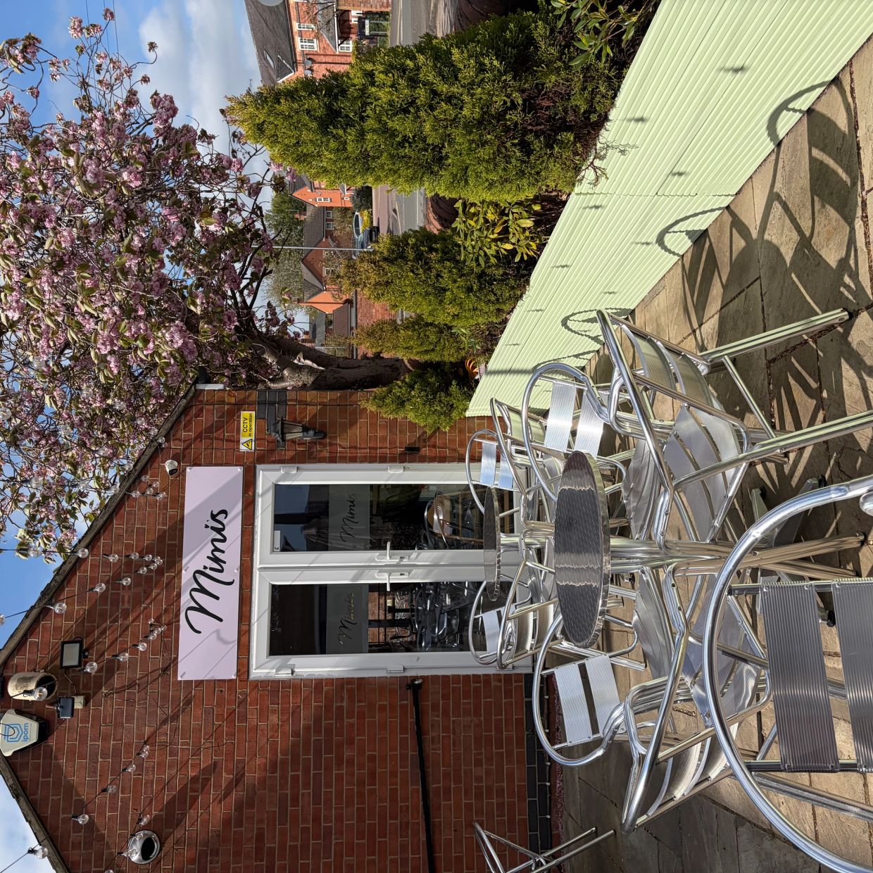Outdoor seating area at Mimi's café with metal chairs and tables under a blossoming tree.