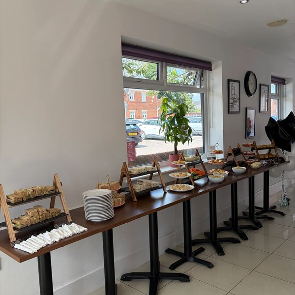 A buffet table with plates and food items set up near a window in a bright room.