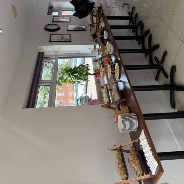 A buffet table with plates and food items set up near a window in a bright room.