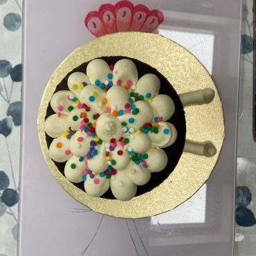 Chocolate cake topped with white frosting and colorful sprinkles on a gold base.